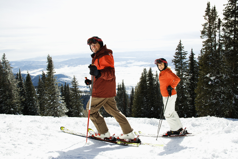 Side view of skiers on a snowy ski slope with trees and valley in background.