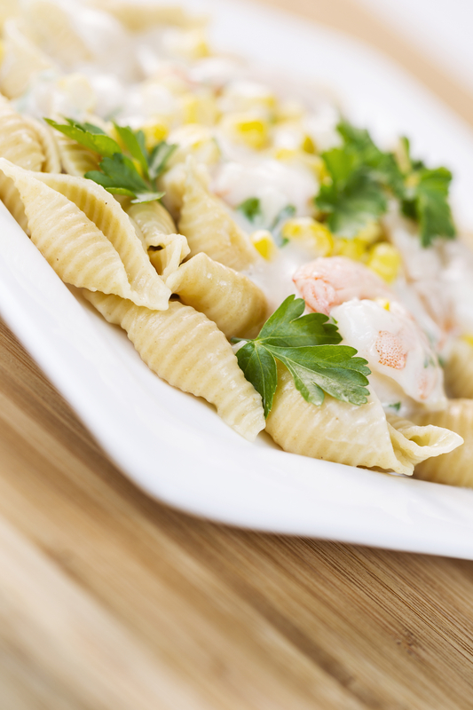 alfredo pasta made of whole wheat shells, shrimp and parsley on white dish with natural bamboo wood underneath